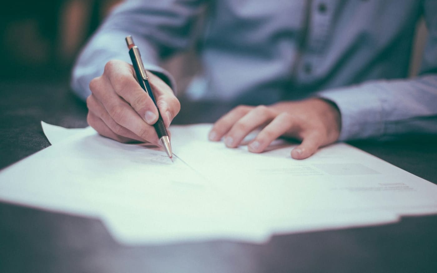 Main signant un document avec un stylo sur un bureau en bois